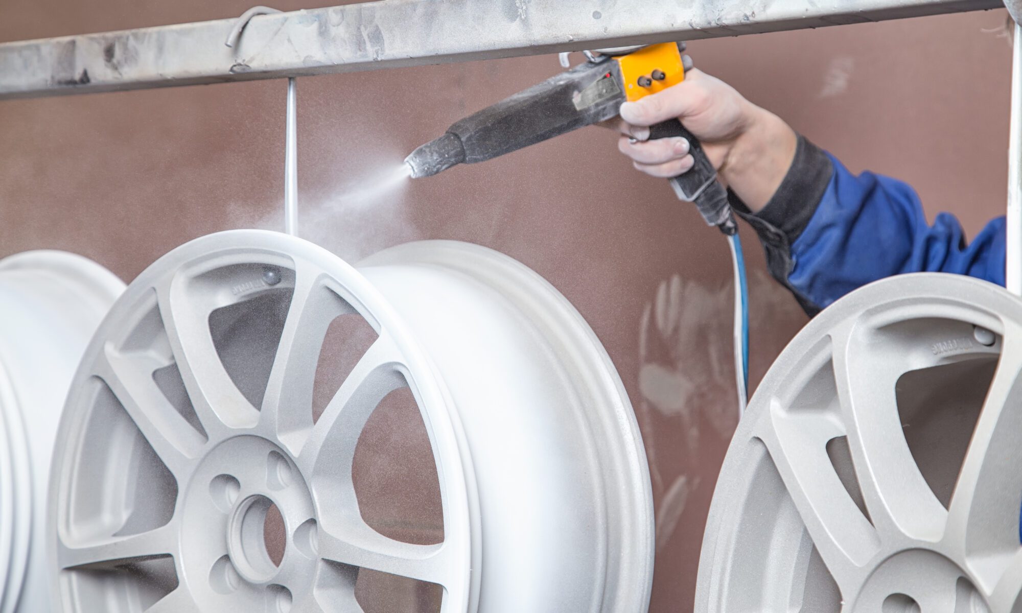 A person spraying a powder-coating gun onto a metal wheel.