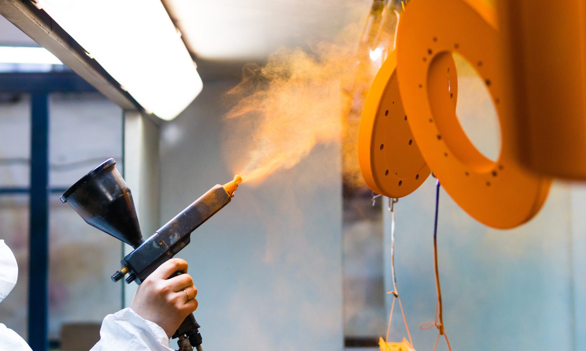 A person powder coats a metal object.