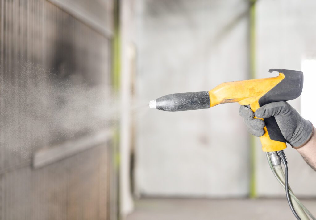 A powder coating gun spraying white powder on an object.