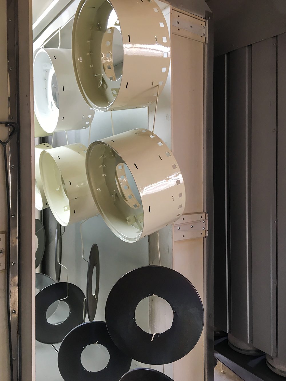 Large round metal products coming out of a powder-coating bake room.